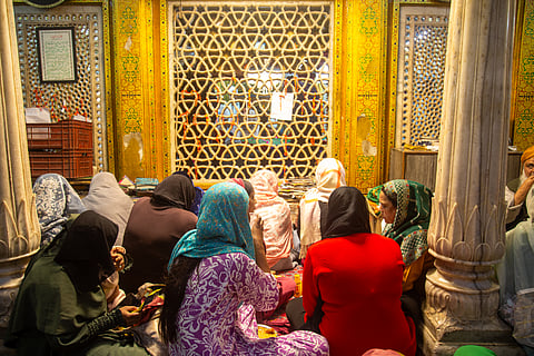 A group of women seated near the wall surrounding the mazar of Khwaja Nizamuddin Auliya at Nizamuddin Dargah. Women are not allowed to enter the mazar.