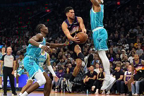 Phoenix Suns guard Devin Booker drives between Charlotte Hornets forward Moussa Diabate, guard Josh Green (10) and forward Miles Bridges during the first half of an NBA basketball in Phoenix.