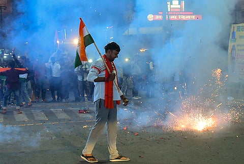 A man carrying the national flag walks past fireworks during celebrations after India defeated New Zealand to win the ICC Men's T20 World Cup 2026 final cricket match, in Patna.