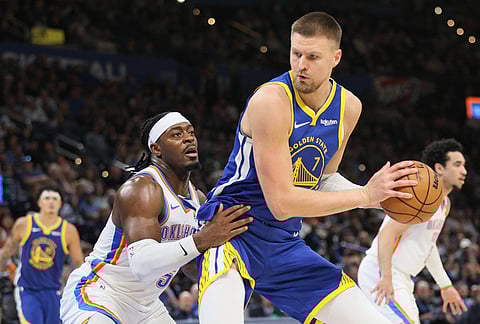 Golden State Warriors center Kristaps Porzingis (7) looks for an outlet against Oklahoma City Thunder guard Luguentz Dort, left, during the second half of an NBA basketball game in Oklahoma City. 
