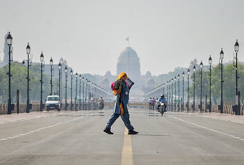 A woman covers her head with a cloth while crossing Kartavya Path on a hot afternoon, in New Delhi.