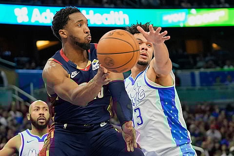 Cleveland Cavaliers guard Donovan Mitchell, left, passes the ball past Orlando Magic forward Noah Penda during the second half of an NBA basketball game in Orlando, Fla.
