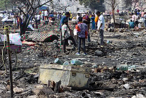 People gather near the wreckage after a fire broke out near a fish market on Wednesday, in Matiala village, Uttam Nagar. As many as 23 fire tenders were deployed to control the fire, which spread across an area of about four acres, officials said. 