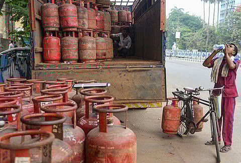 A worker drinks water while carrying a liquefied petroleum gas (LPG) cylinder for delivery, in Kolkata. 