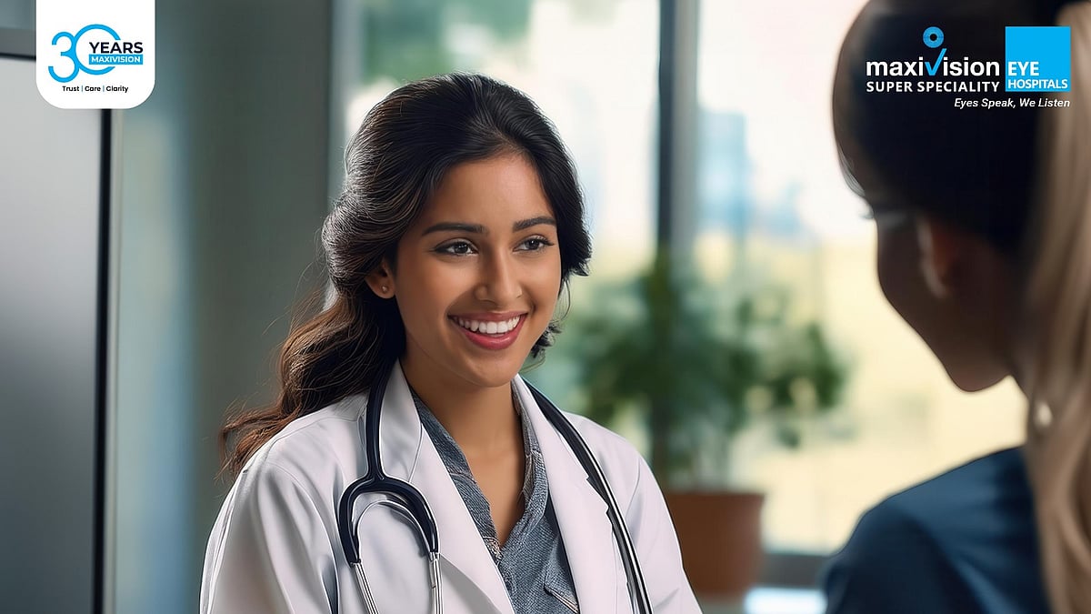 A smiling female doctor in a white lab coat and stethoscope talking to a patient.