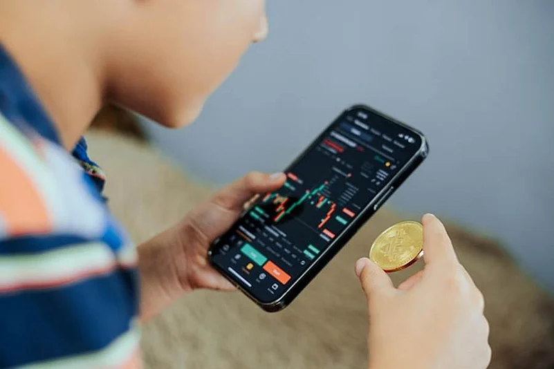 Person holding a crypto coin and checking trading charts on a smartphone
