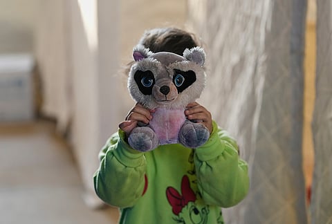 A displaced girl holds a stuffed toy to cover her face from a photographer while standing inside the Camille Chamoun Sports City Stadium, which has been turned into a shelter for people displaced by Israeli airstrikes in southern Lebanon and Dahiyeh, Beirut's southern suburbs, in Beirut, Lebanon, Tuesday, March 10, 2026. 