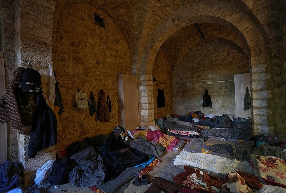 A displaced migrant man who was among others who fled Israeli strikes in southern and eastern Lebanon and Beirut's southern suburbs checks his mobile phone as he sits on a mattress at Saint Joseph Church, which has been turned into a shelter for displaced migrants, mostly from African nations, in Beirut, Wednesday, March 11, 2026.  - | Photo: AP/Hussein Malla