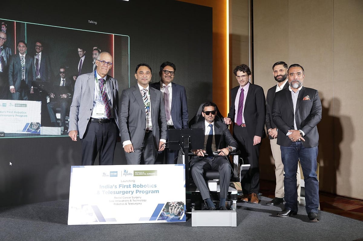 A group of men posing with a robotics and telesurgery medical console at a symposium.