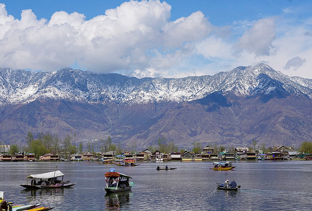 Shikaras ferry tourists on the Dal Lake with snow-clad mountains in the backdrop, in Srinagar. - | Photo: PTI