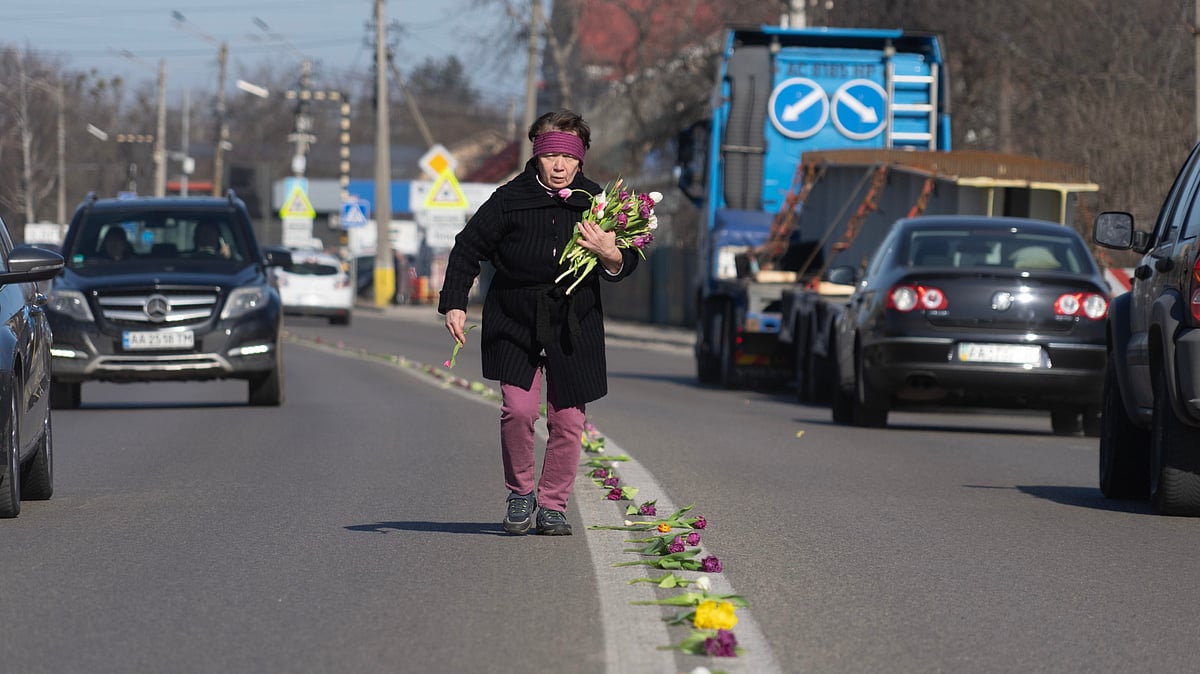A villager lays flowers on a road in the village of Novi Petrivtsi close to capital Kyiv, Ukraine, Thursday, March 12, 2026, ahead of a funeral procession for a Ukrainian army soldier who was killed in a battle with Russian troops. -  Credit: AP Photo/Efrem Lukatsky