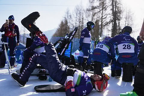 Mike Schultz, of the United States, stretches during warmup before the start of the snowboard cross competitions at the 2026 Winter Paralympics, in Cortina d'Ampezzo, Italy.