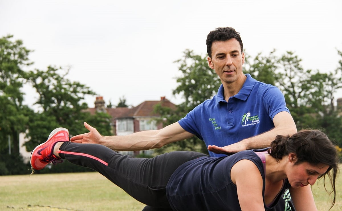 Trainer assisting woman with leg exercise during outdoor rehabilitation