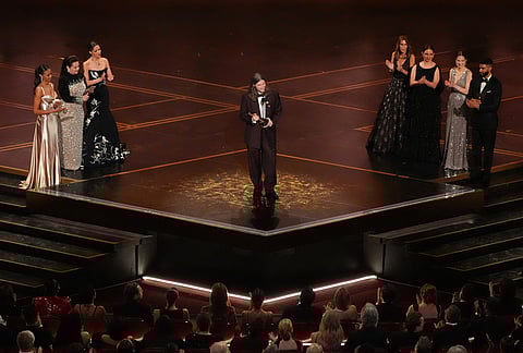 Ludwig Göransson, center, accepts the award for music (original score) for "Sinners" during the Oscars at the Dolby Theatre in Los Angeles. Melissa McCarthy, from left, Rose Byrne, Kristen Wiig, Maya Rudolph, Ellie Kemper look on.