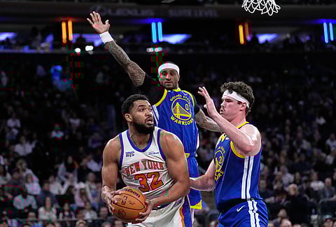 New York Knicks' Karl-Anthony Towns, left, looks to pass around Golden State Warriors defenders during the second half of an NBA basketball game in New York.