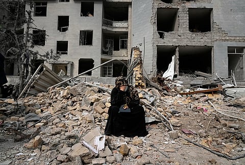 A woman sits on rubble across from a residential building damaged last Sunday during the U.S.-Israeli air campaign in Tehran, Iran, Thursday, March 12, 2026. 