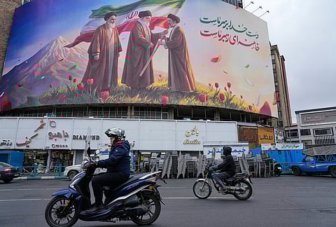 Motorbikes drive past a billboard depicting Iran’s late Supreme Leader Ayatollah Ali Khamenei, center, handing the country’s flag to his son and successor Ayatollah Mojtaba Khamenei, right, as the late revolutionary founder Ayatollah Ruhollah Khomeini stands at left, in a square in downtown Tehran, Iran, Tuesday, March 10, 2026. 