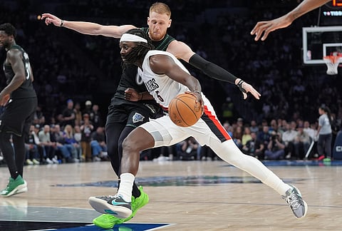 Portland Trail Blazers guard Jrue Holiday (5) works toward the basket as Minnesota Timberwolves guard Donte DiVincenzo (0) defends during the second half of an NBA basketball game, in Minneapolis.
