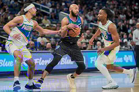 Orlando Magic guard Jevon Carter, center, makes a move to get through Indiana Pacers forward Obi Toppin, left, and guard Aaron Nesmith (23) during the first half of an NBA basketball game in Orlando, Fla.