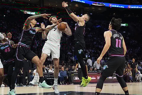 San Antonio Spurs center Luke Kornet (7) fights for control of the ball against Miami Heat center Kel'el Ware, left, and guard Tyler Herro, second from right, during the first half of an NBA basketball game, in Miami.
