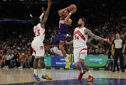 Phoenix Suns guard Devin Booker drives between Toronto Raptors guard Jamal Shead (23) and forward Sandro Mamukelashvili during the first half of an NBA basketball game in Phoenix.
