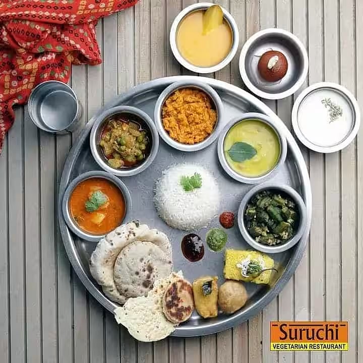 An Indian vegetarian thali with rice, rotis, diverse curries, dal, and sweets on a silver platter.