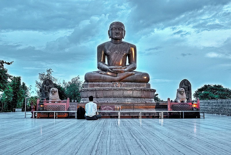 Large seated Jain statue in temple courtyard under cloudy sky