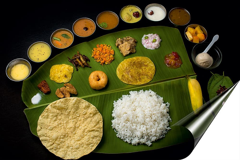 A South Indian thali served on a banana leaf with rice, papadum, vada, and various side dishes.