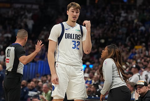 Dallas Mavericks forward Cooper Flagg, center, holds up his elbow for trainer Jana Austin to tend to after he fell following a collision with Denver Nuggets forward Cameron Johnson in pursuit of a long pass in the second half of an NBA basketball game in Denver.
