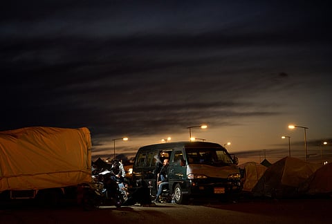 A man who fled Israeli strikes in southern Lebanon smokes in his van with his family outside a tent used as a shelter in Beirut, Lebanon.
