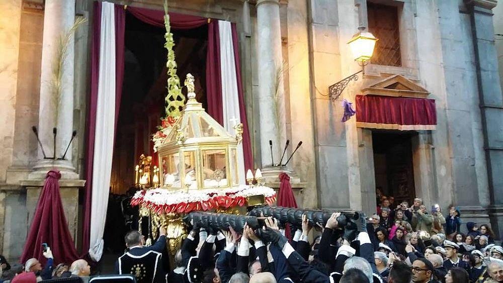 Religious procession carrying a sacred float outside a historic church in Italy.