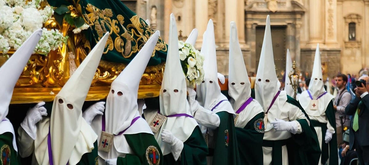 Penitents in white robes and pointed hoods during a Holy Week religious procession.