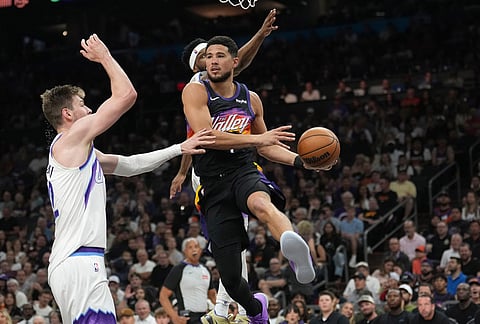 Phoenix Suns guard Devin Booker, right, looks to pass the ball against Utah Jazz forward Kyle Filipowski, left, during the first half of an NBA basketball game in Phoenix.
