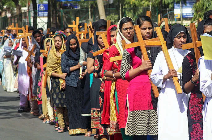 Women in colorful clothing and headscarves carry large wooden crosses in a procession