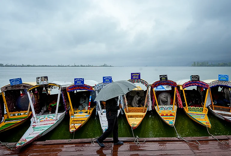A man walks past shikaras holding an umbrella during rainfall at Dal Lake, in Srinagar. - | Photo: PTI/S Irfan