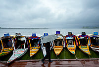 Day In Pics: March 30, 2026 | Photo: PTI/S Irfan : A man walks past shikaras holding an umbrella during rainfall at Dal Lake, in Srinagar.