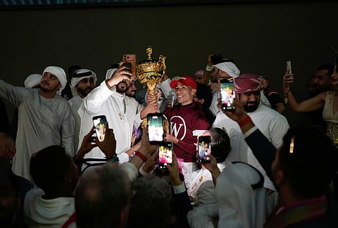 Magnitude's jockey Jose Ortiz, center, poses for photos while holding the trophy after winning the $12 million Dubai World Cup horse race over 2,000 meters (10 furlongs) at Meydan Racecourse in Dubai, United Arab Emirates.