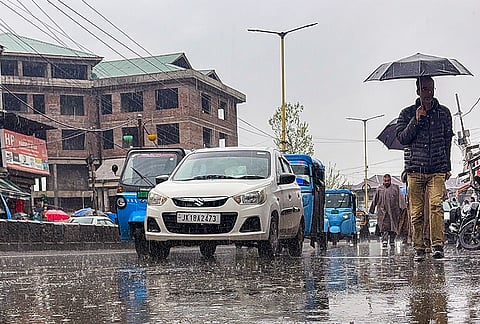 People walk with umbrellas as vehicles ply on a rain-soaked road during rainfall, in Anantnag, Jammu and Kashmir.