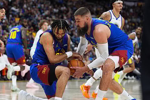 Denver Nuggets guard Jamal Murray, left, falls to a knee after running into center Jonas Valančiūnas in pursuit of a rebound in the second half of an NBA basketball game against the Golden State Warriors in Denver.