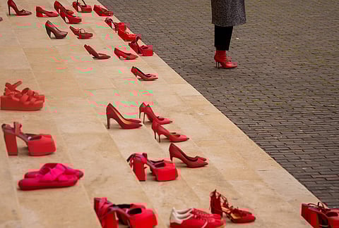 A woman stands next to pairs of red shoes, a symbol of solidarity with victims of domestic violence, during an awareness event in Bucharest, Romania where organisers said that one woman dies weekly in Romania due to domestic violence. 
