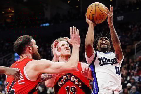 Sacramento Kings' Malik Monk (0) shoots as Toronto Raptors' Sandro Mamukelashvili (54) and Jakob Poeltl (19) defend during second half NBA basketball action in Toronto.