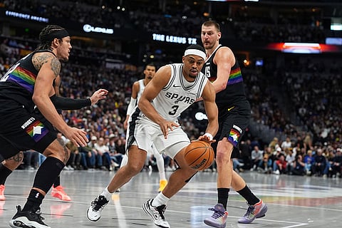 San Antonio Spurs guard Keldon Johnson, center, pursues a loose ball with Denver Nuggets forward Aaron Gordon, left, and center Nikola Jokic during the first half of an NBA basketball game in Denver.