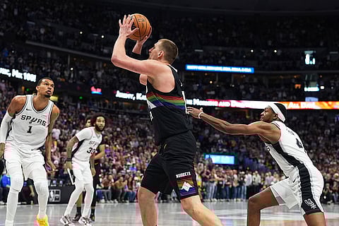 Denver Nuggets center Nikola Jokic drives between San Antonio Spurs center Victor Wembanyama, left, and guard De'aaron Fox, right, to hit a basket late in overtime of an NBA basketball game in Denver.
