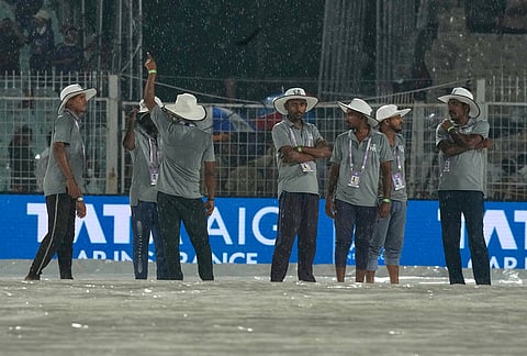 Ground staff stand on rain covers as it rains during the Indian Premier League cricket match between Kolkata Knight Riders and Punjab Kings in Kolkata.
