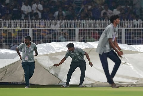 Ground staff pull in rain covers to the field as it rains during the Indian Premier League cricket match between Kolkata Knight Riders and Punjab Kings in Kolkata.