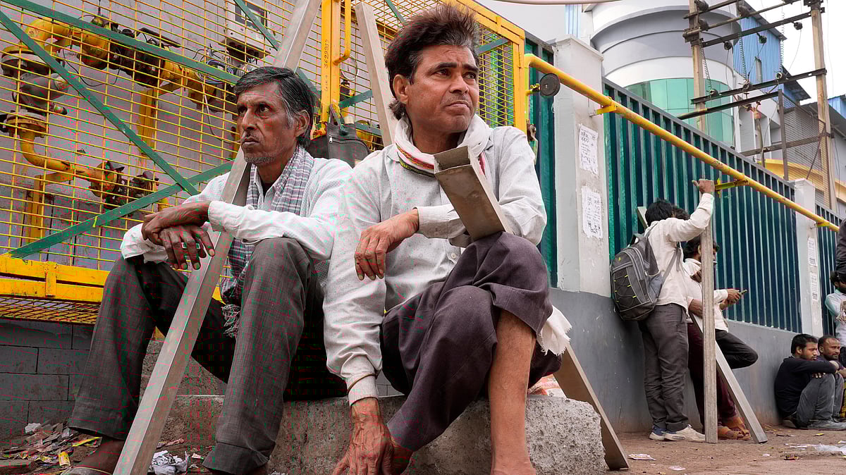 Workers stand at Noida’s informal hiring hub with tools, paint brushes, measuring tapes, gauging trowels and wooden floats, waiting for work - SURESH K PANDEY