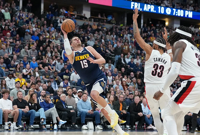 Denver Nuggets center Nikola Jokić, left, falls as he puts up a shot after being fouled by Portland Trail Blazers forward Toumani Camara, back right, as center Robert Williams III looks on in the second half of an NBA basketball game in Denver. - | Photo: AP/David Zalubowski