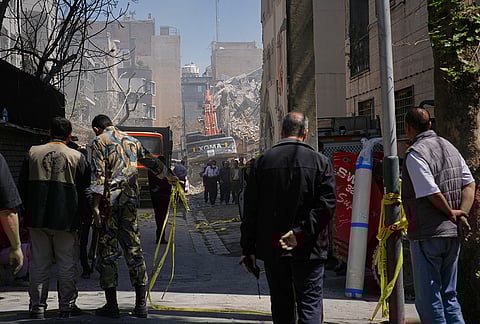 Bystanders watch from a distance as rescue teams and first responders work at the site of a strike that, according to a security official at the scene, destroyed half of the Khorasaniha Synagogue and nearby residential buildings in Tehran, Iran, Tuesday, April 7, 2026. 