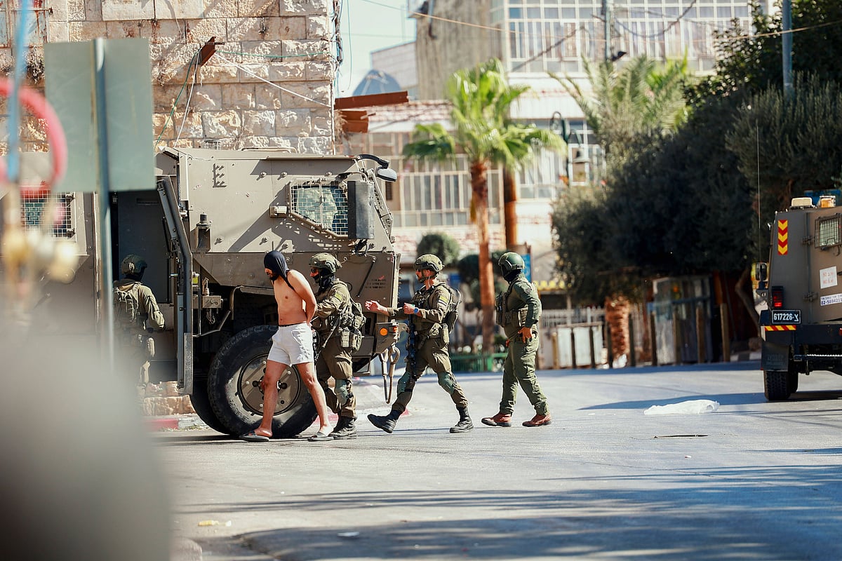 Israeli Raid In Al Birah West Bank Israeli soldiers escort a detained man near a military vehicle in Al Birah, West Bank on October 7, 2025 - Credit: IMAGO / Middle East Images