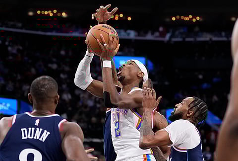 Oklahoma City Thunder guard Shai Gilgeous-Alexander, center, shoots as Los Angeles Clippers guard Kris Dunn, left, and forward Derrick Jones Jr., right, defend during the first half of an NBA basketball game in Inglewood, California.